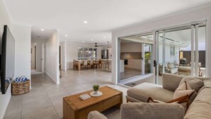 A modern living room with a sofa, coffee table, and a dining area with chairs and a table. - Mooloolaba Canal Retreat with Pool, Sleeps 12 (Mooloolaba)