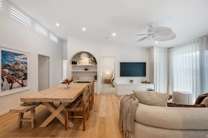 A modern living room with a wooden dining table, sofa, and TV. - Luxury Top Floor Apartment with Ocean Views (Coolum Beach)