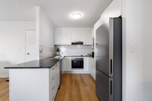 A modern kitchen with white cabinetry, a black countertop, a built-in oven, and a stainless steel refrigerator. - 2 BR Ocean-view apartment at Mirage Resort (Alexandra Headland)