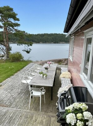 Une terrasse en bois avec coin salon extérieur, un barbecue et une vue sur un lac et une forêt.