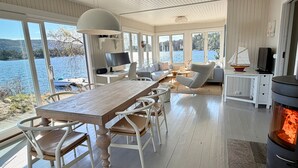 A spacious room with a wooden dining table, white chairs, a TV, and a fireplace. - Waterfront Retreat - Frontline Oslofjord | Small boat included | Fireplace (Akershus)