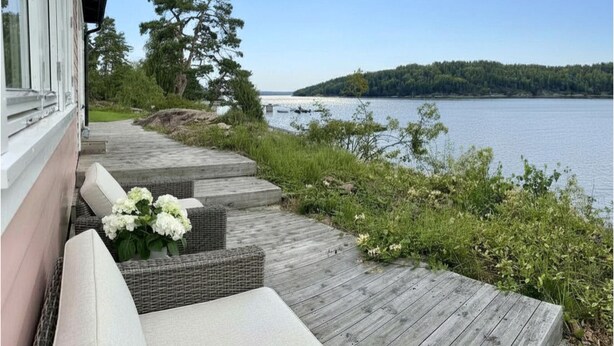 A wooden deck with outdoor seating, overlooking a lake and forested island. - Waterfront Retreat - Frontline Oslofjord | Small boat included | Fireplace (Akershus)