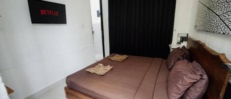A bedroom with a bed, a wall-mounted Netflix sign, a door, and a wall art piece.