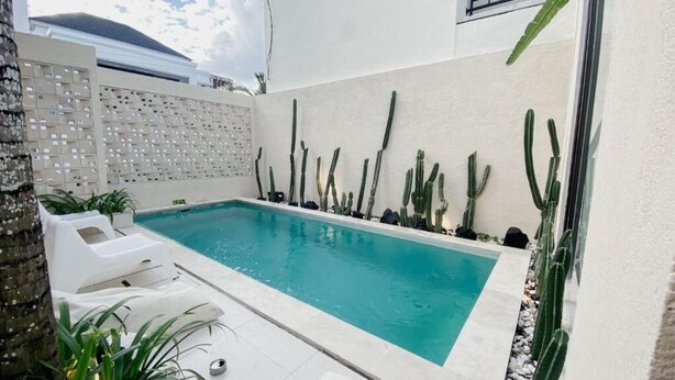 A swimming pool with white lounge chairs, surrounded by cacti and a white wall with a patterned design. - Escotel Tempekan Canggu (Tibubeneng)