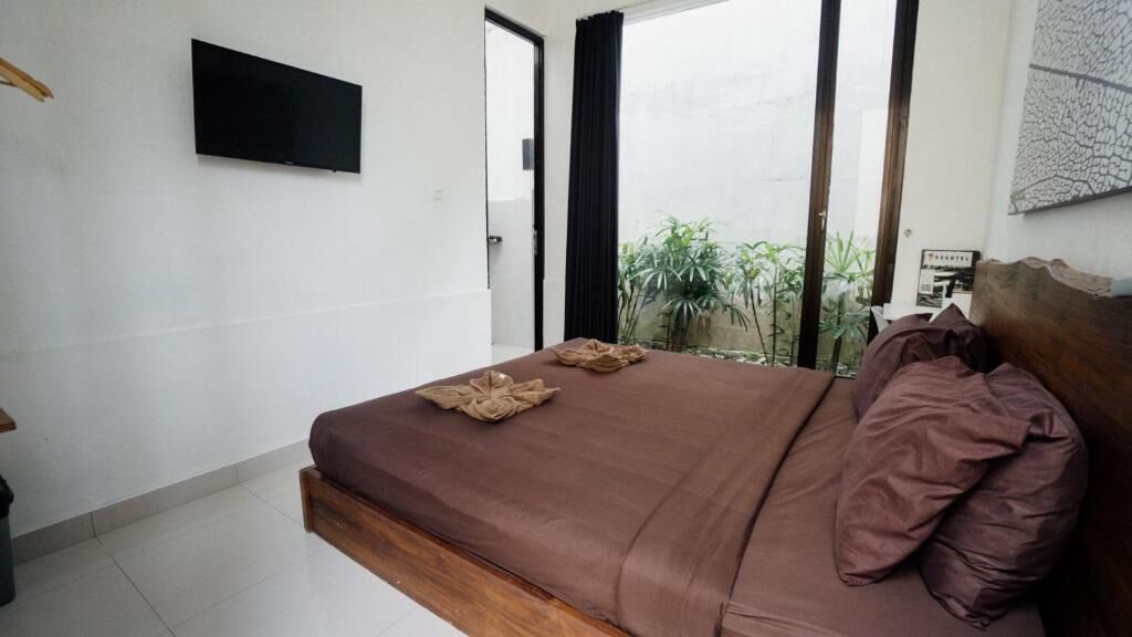 A bedroom with a bed, a flat-screen TV, and a view of greenery outside.