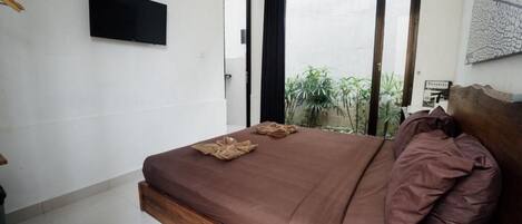 Quarto com cama, televisão de tela plana e vista para o verde lá fora.