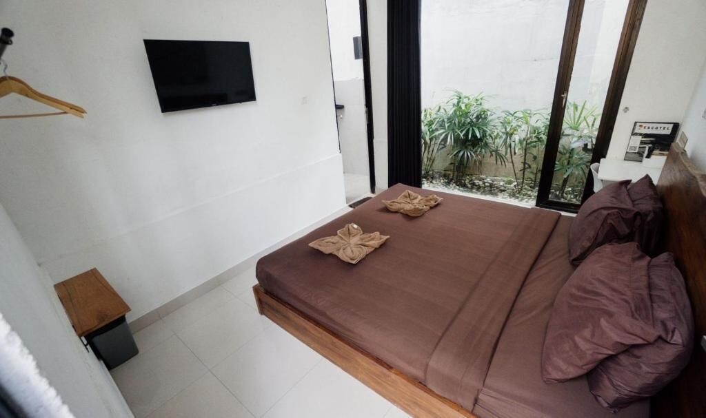 A bedroom with a bed, a TV mounted on the wall, and a view of greenery outside.