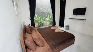 A bedroom with a bed, curtains, a TV, and a window with plants. - Escotel Tempekan Canggu (Tibubeneng)