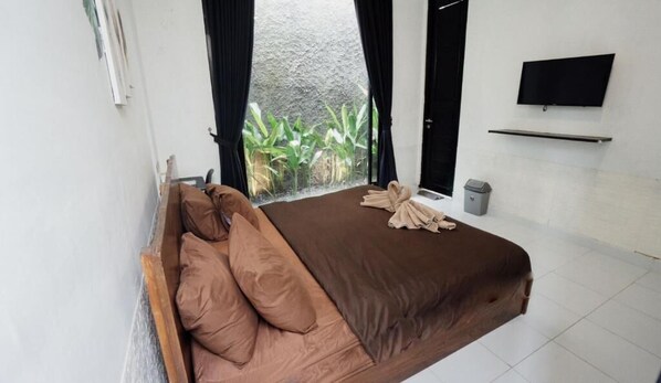Un dormitorio con cama, cortinas, televisor y ventana con plantas.