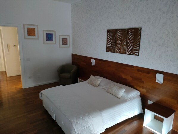 Ein Schlafzimmer mit einem hölzernen Kopfteil, einem Bett mit weißer Bettwäsche, einem Sessel und einem Nachttisch.