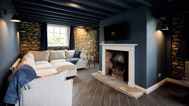 Una sala de estar con una pared de piedra, una chimenea, un sofá y un televisor montado en la pared.