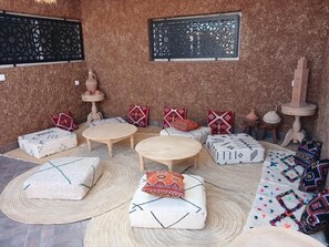 Una habitación con pared de diseño, una mesa redonda de madera, varios otomanes y cojines decorativos.