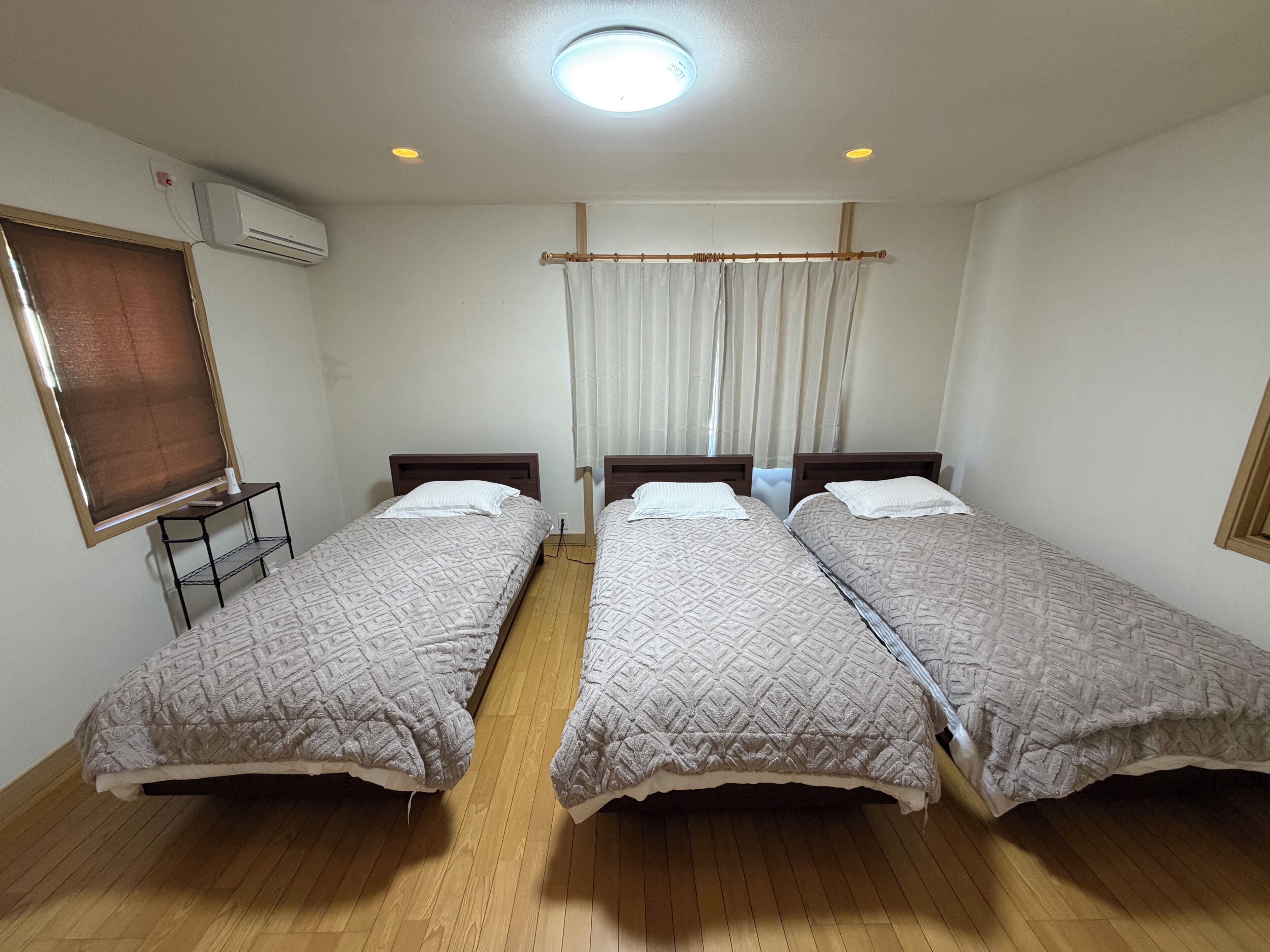 Une chambre avec deux lits simples, un plancher en bois, un luminaire au plafond et une fenêtre avec des rideaux.