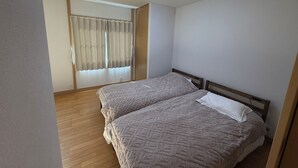 Ein Schlafzimmer mit zwei Betten, Holzboden, Deckenleuchte und einem Fenster mit Vorhängen.