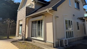 Ein zweistöckiges Haus mit geneigtem Dach, großen Fenstern und einer sichtbaren Klimaanlage.