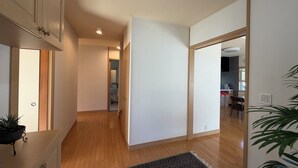 Ein Korridor mit Holzboden, einem Blumentopf, einem gemusterten Teppich und Blick in einen Küchenbereich.