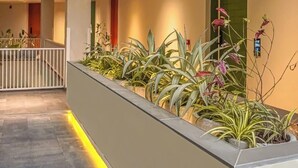 Et moderne hotelindretning med en central plantekasse med planter, en balkon på anden sal og et rent, minimalistisk design.