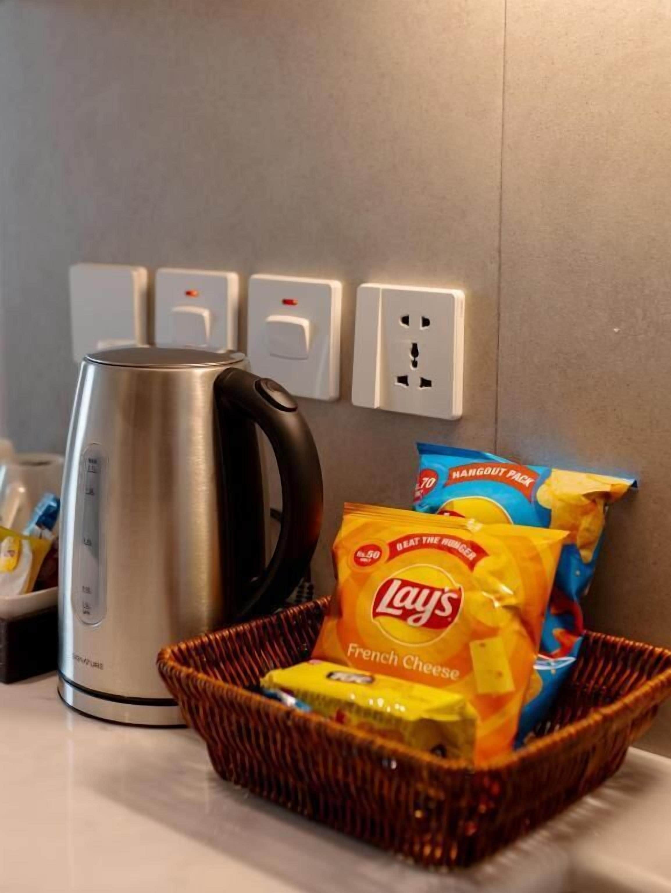 A kitchen counter with a kettle, a basket of snacks, and a power outlet.