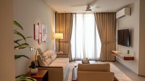 Et hotelværelse med sofa, sofabord, fjernsyn og loftsvifte.