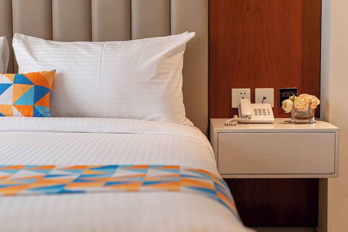 A hotel room with a bed, a nightstand with a phone and a vase of flowers, and a wooden headboard.