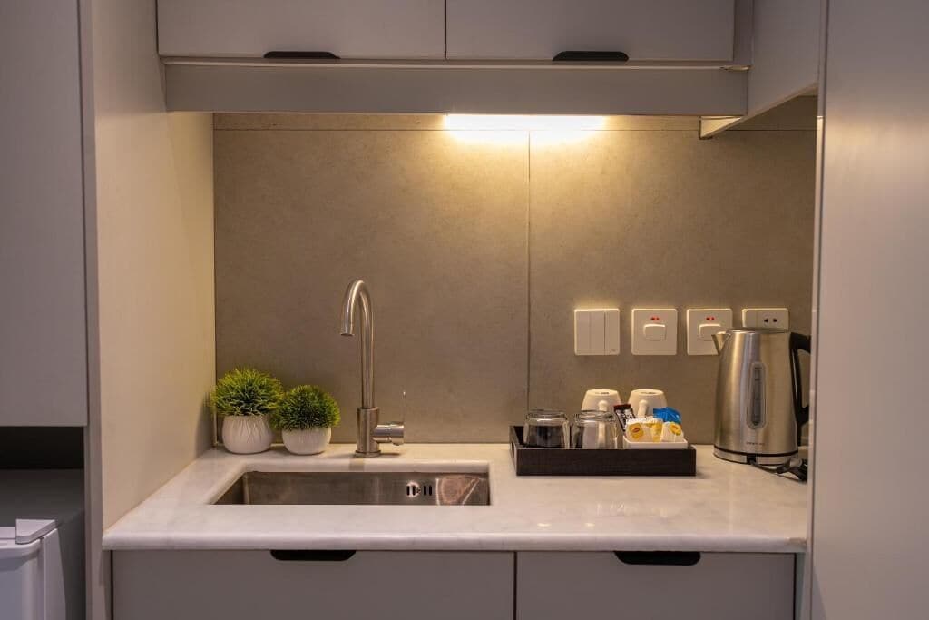 A modern kitchen with a stainless steel sink, a kettle, and a tray with condiments.