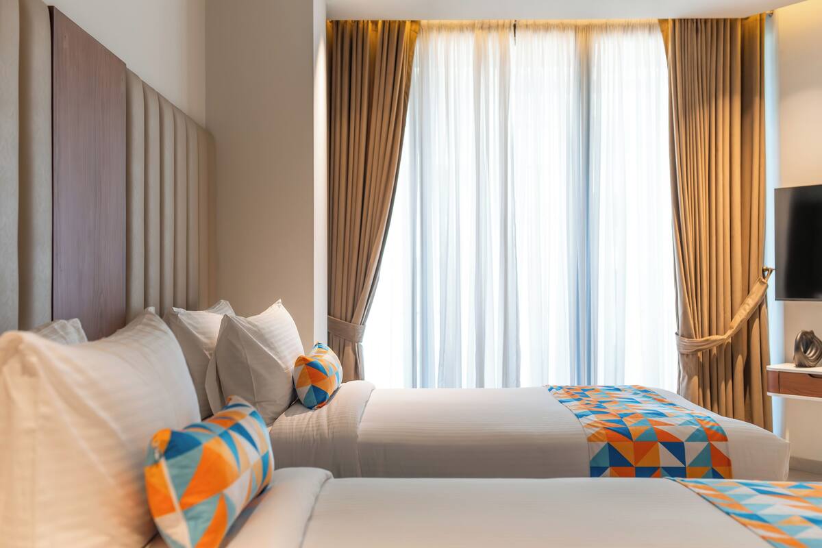 A hotel room with a bed, curtains, a television, and a desk.