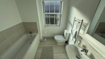Ein Badezimmer mit Badewanne, Toilette, Waschbecken und einem Fenster.