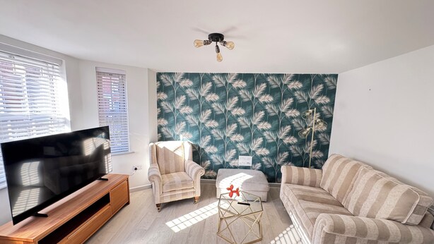 A living room with a TV, a ceiling fan, a patterned wall, a sofa, and a chair.