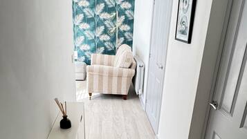 A hallway with a white cabinet, a beige sofa, a teal leaf-patterned wall, and a door with a framed picture.