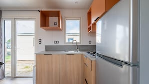 A modern kitchen with a stainless steel refrigerator, wooden cabinets, and a window overlooking a residential area. - Caravan by the sea Blankenberge (Blankenberge)