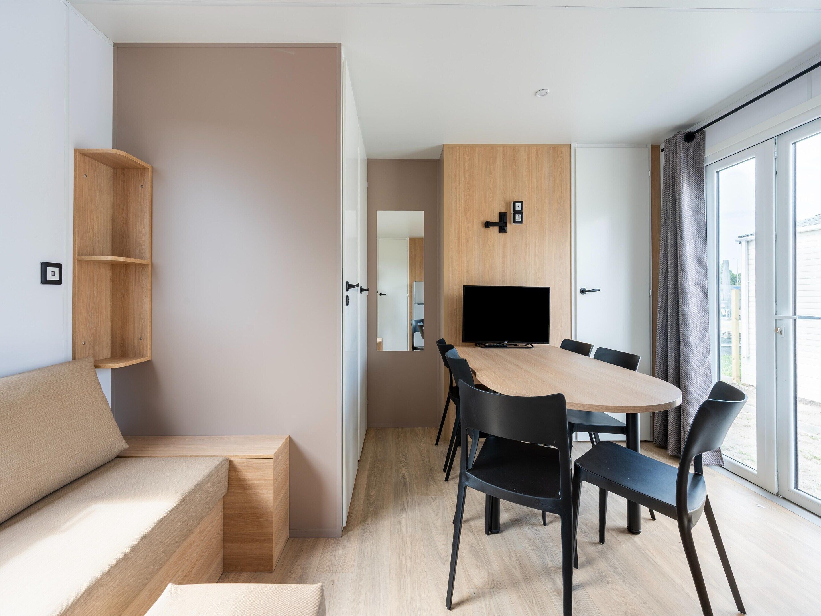 A modern room with a wooden table, black chairs, a TV, and a large window.