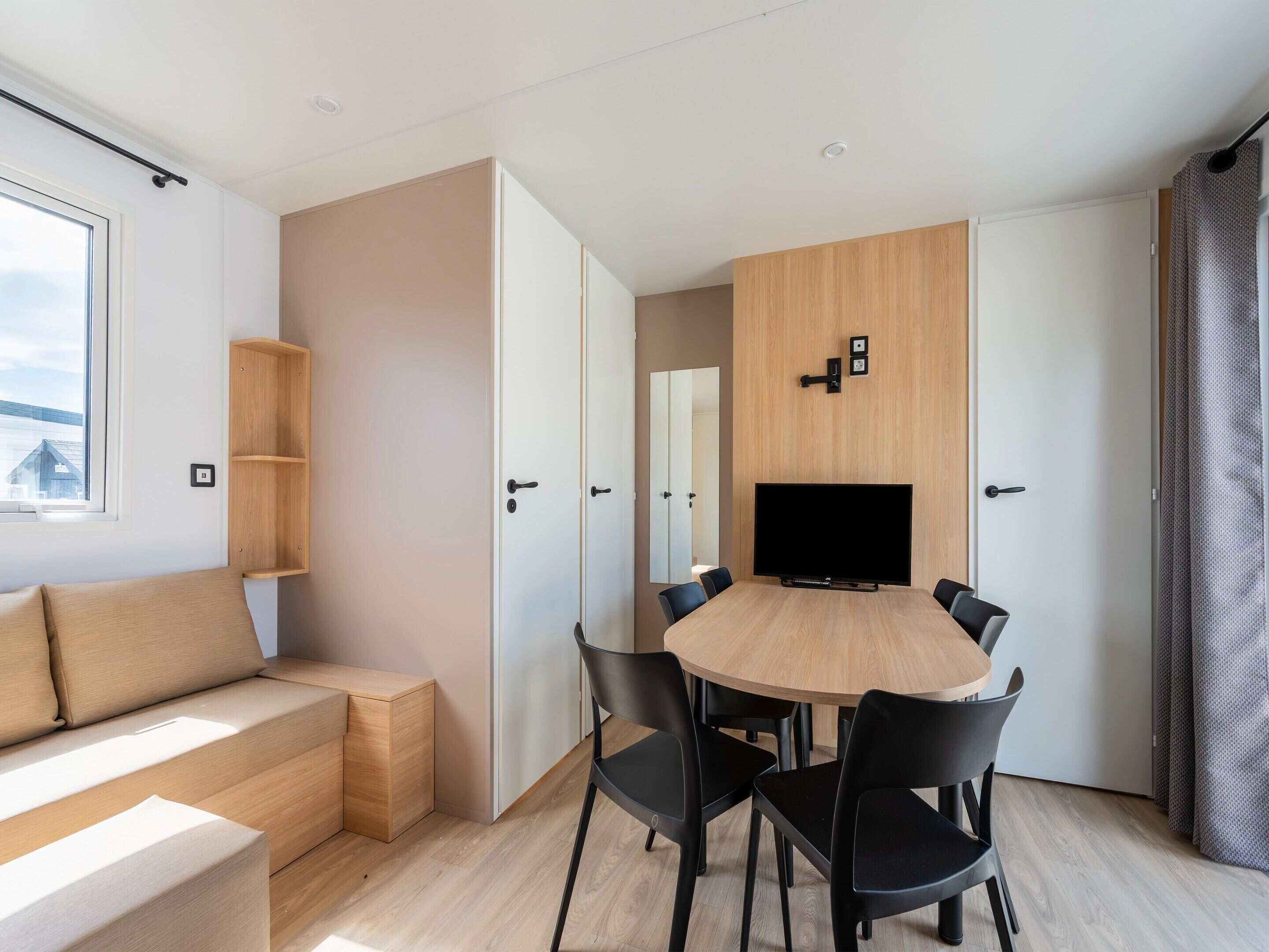Ein modernes Zimmer mit einem Holzesstisch, schwarzen Stühlen, einer Couch und einem an der Wand befestigten Fernseher.