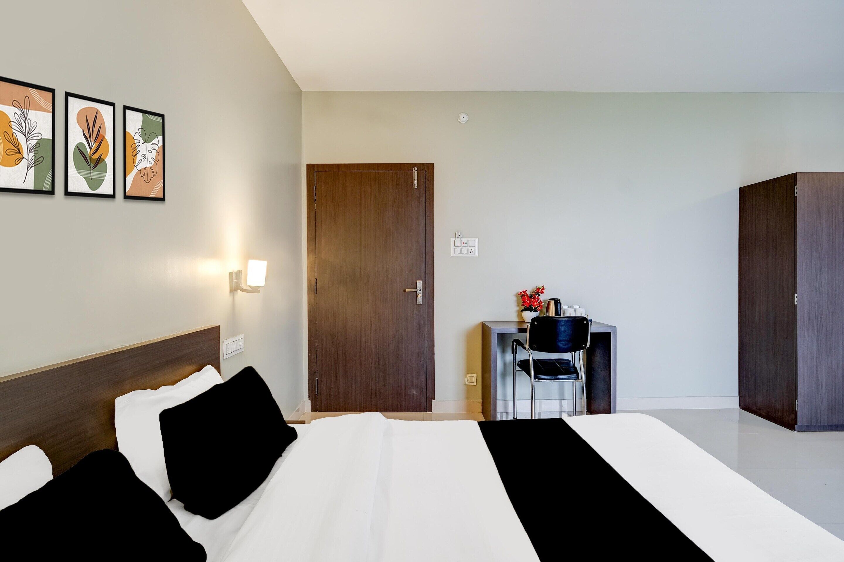 Ein Hotelzimmer mit Bett, Schreibtisch, Stuhl, Kleiderschrank und Wandbildern.