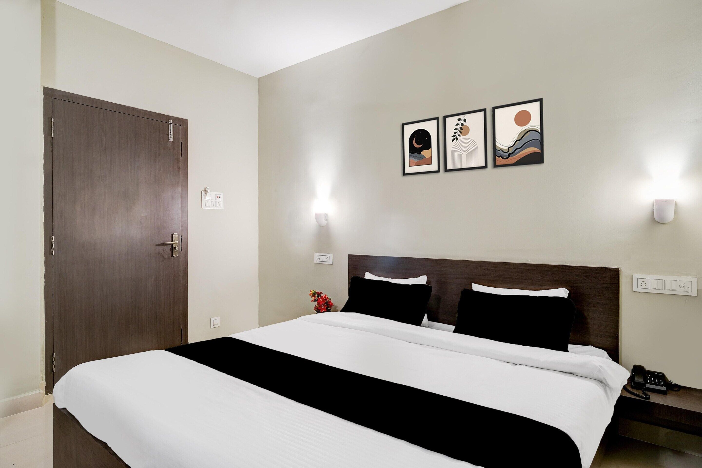 Habitación de hotel con cama, mesita de noche, teléfono y cuadros colgados en la pared.