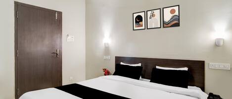 Habitación de hotel con cama, mesita de noche, teléfono y cuadros colgados en la pared.