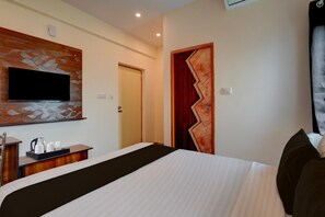 Quarto de hotel com cama, televisão de tela plana presa numa parede decorativa, escrivaninha de madeira com bandeja de objetos e porta com design em zigue-zague.