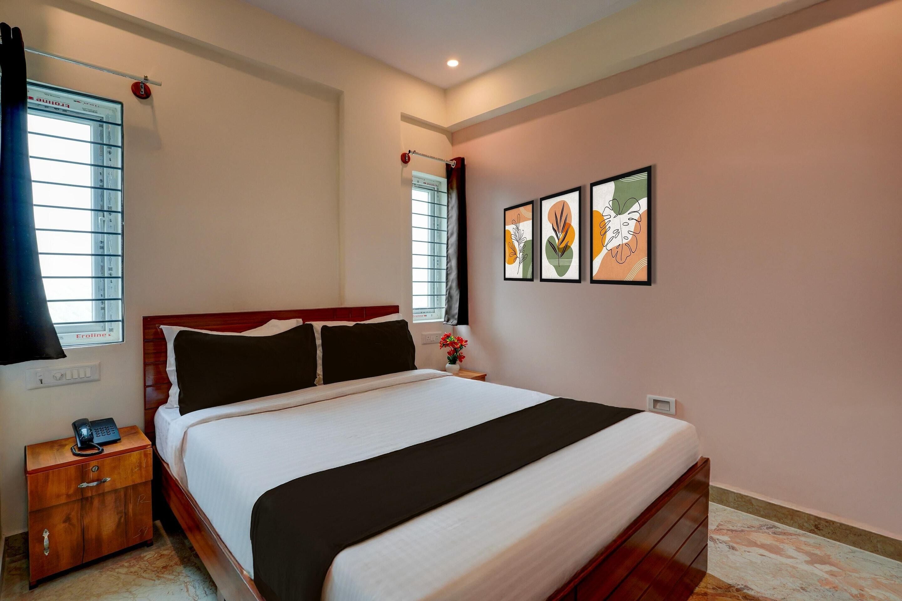 A hotel room with a bed, a nightstand, a window with blinds, and wall art.