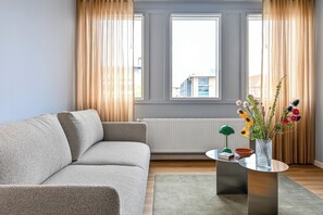 A modern living room with a grey sofa, a round glass coffee table, and a vase with flowers. - The Break Hotel (Herning)