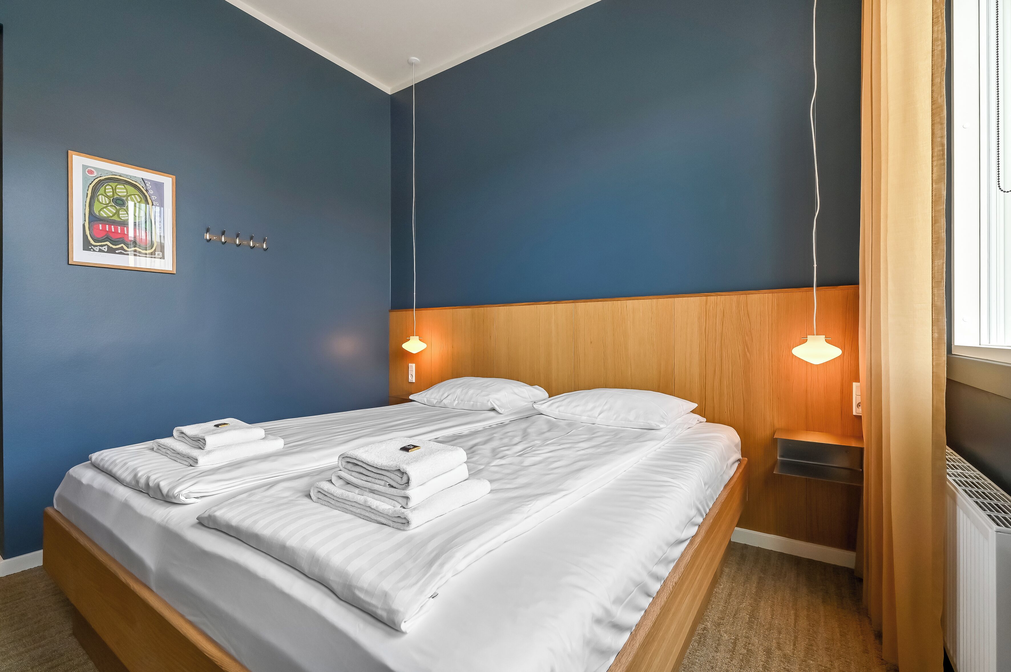 A neatly made bed with white linens, a framed picture on the wall, and a wooden headboard.