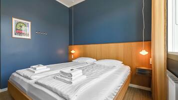 A neatly made bed with white linens, a framed picture on the wall, and a wooden headboard.