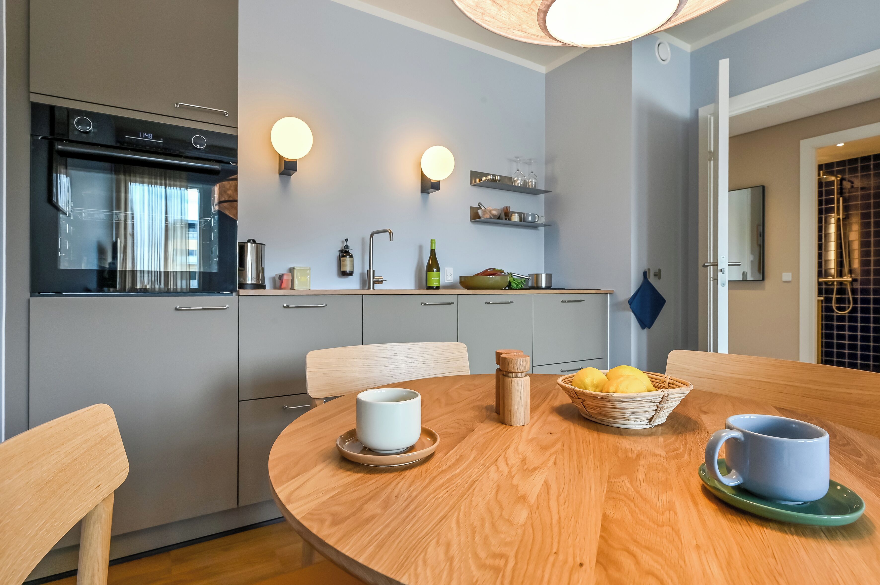 Une cuisine moderne équipée d’un four encastré, une table à manger avec des chaises et un panier de citrons.