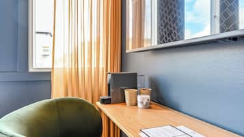 Une pièce avec un bureau en bois, une chaise verte, une fenêtre avec des stores et un téléviseur fixé au mur.