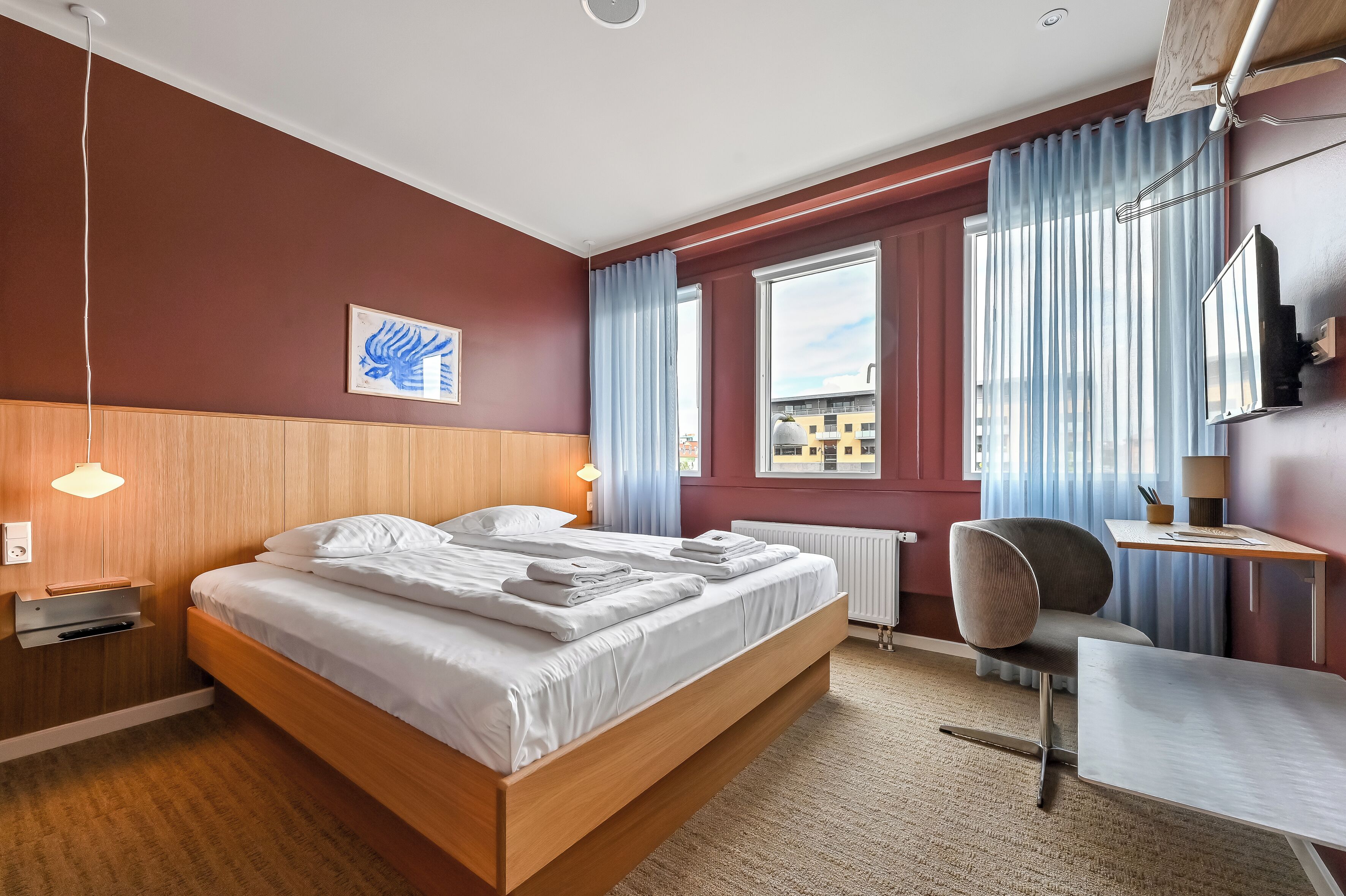 Ein Hotelzimmer mit einem hölzernen Bett, einem Schreibtisch, einem Sessel, einer Heizung und einem Fenster mit Vorhängen.