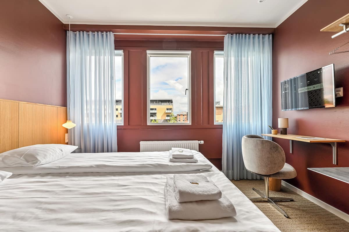 A hotel room with two beds, a desk, a chair, a TV, and a window with curtains.