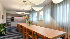 A modern kitchen with a wooden dining table, pendant lights, and a view of the city. - The Break Hotel (Herning)