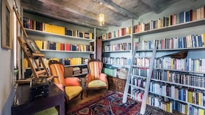 A room with bookshelves, a ladder, a chair, and a patterned rug. - Villa Francescon (Borgo Valbelluna)