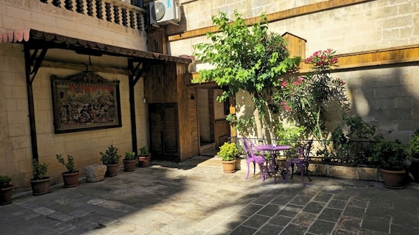 Un patio al aire libre con una pérgola de madera, plantas en macetas y una mesa con sillas.