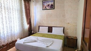 A hotel room with a bed, a nightstand, a framed picture on the wall, and a window with curtains. - Gülizar Konukevi (Şanlıurfa)