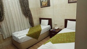 A hotel room with two single beds, a nightstand with a phone, and a painting on the wall. - Gülizar Konukevi (Şanlıurfa)