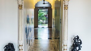 A hallway with ornate columns, patterned floor tiles, and a decorative archway leading to a bright room.